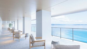 Un balcón moderno y amplio con vistas al mar, que incluye sillas de madera y una mesita.