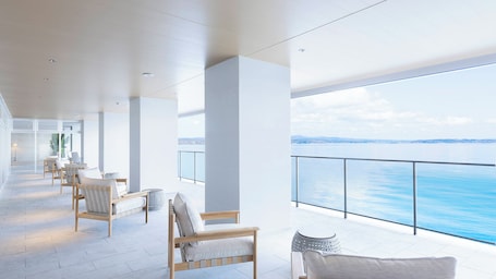 A modern, spacious balcony with a view of the sea, featuring wooden chairs and a small table.