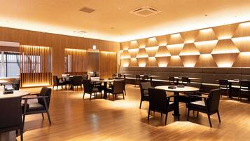 Un restaurante moderno con suelo de madera, diversas opciones de asientos que incluyen mesas y cabinas, y una pared con un diseño geométrico.