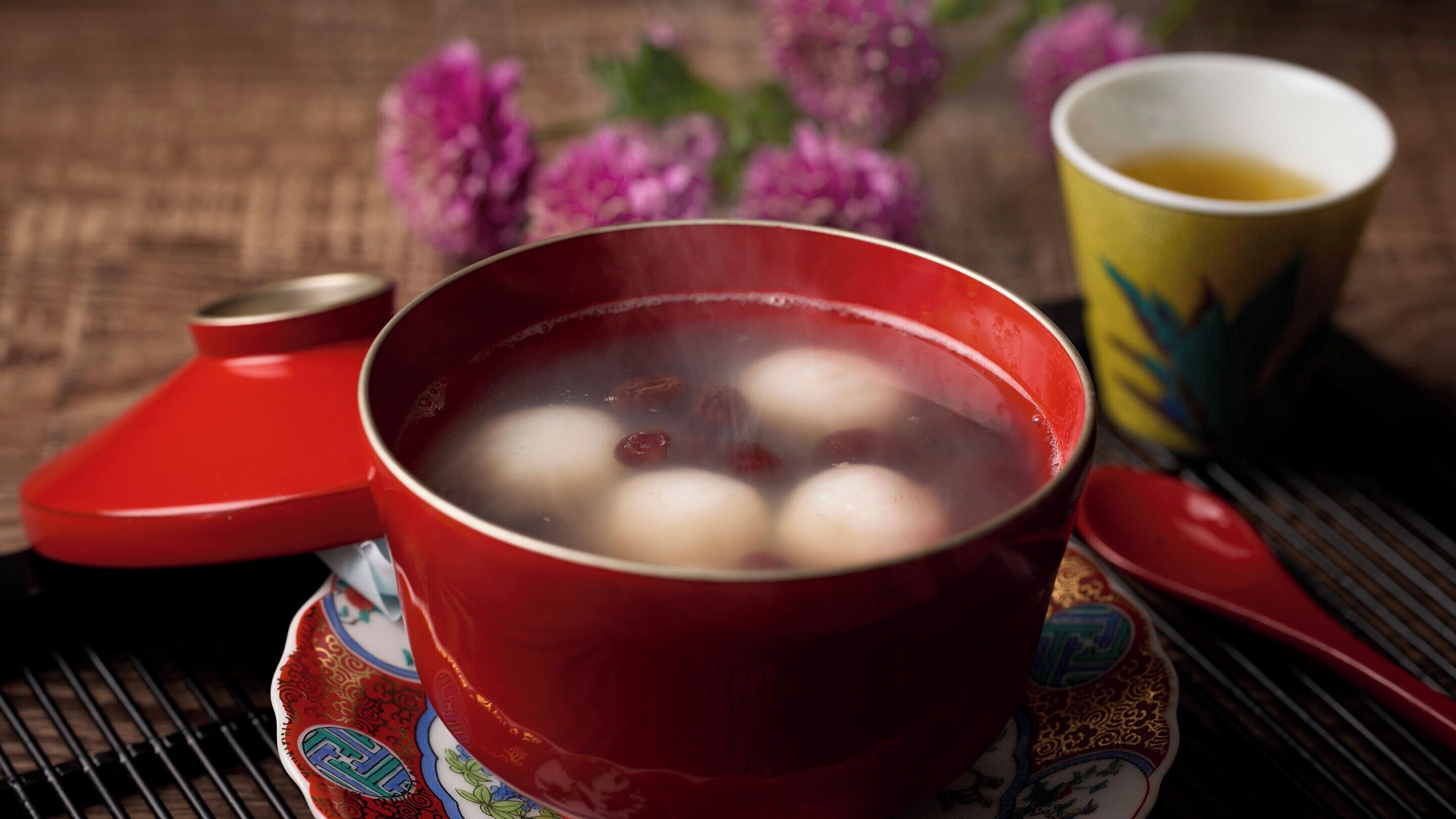 A red bowl with round items and a cup of tea on a table.