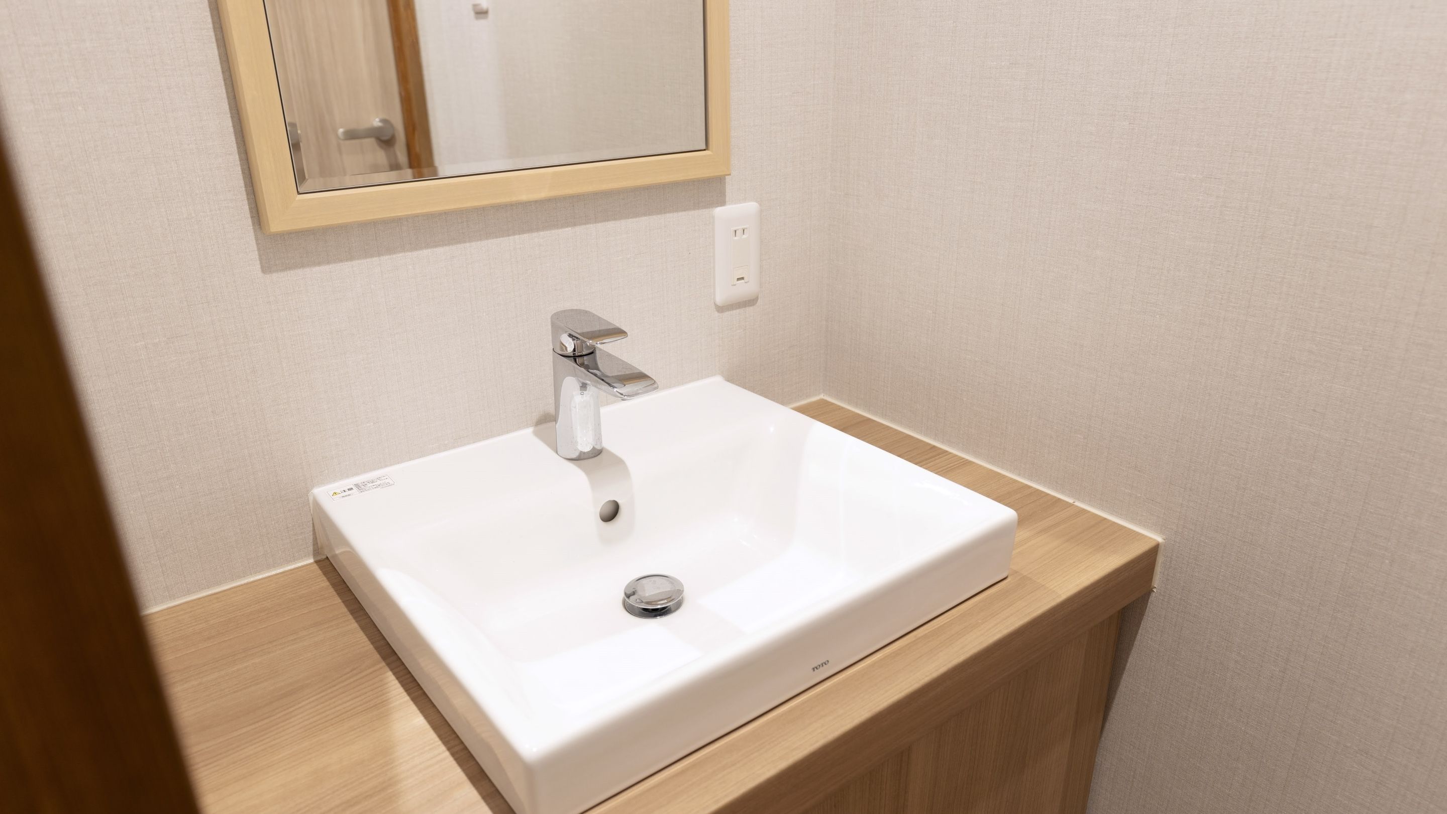 Un baño con un lavamanos blanco, un espejo y un tocador de madera.