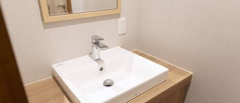 Un baño con un lavamanos blanco, un espejo y un tocador de madera.