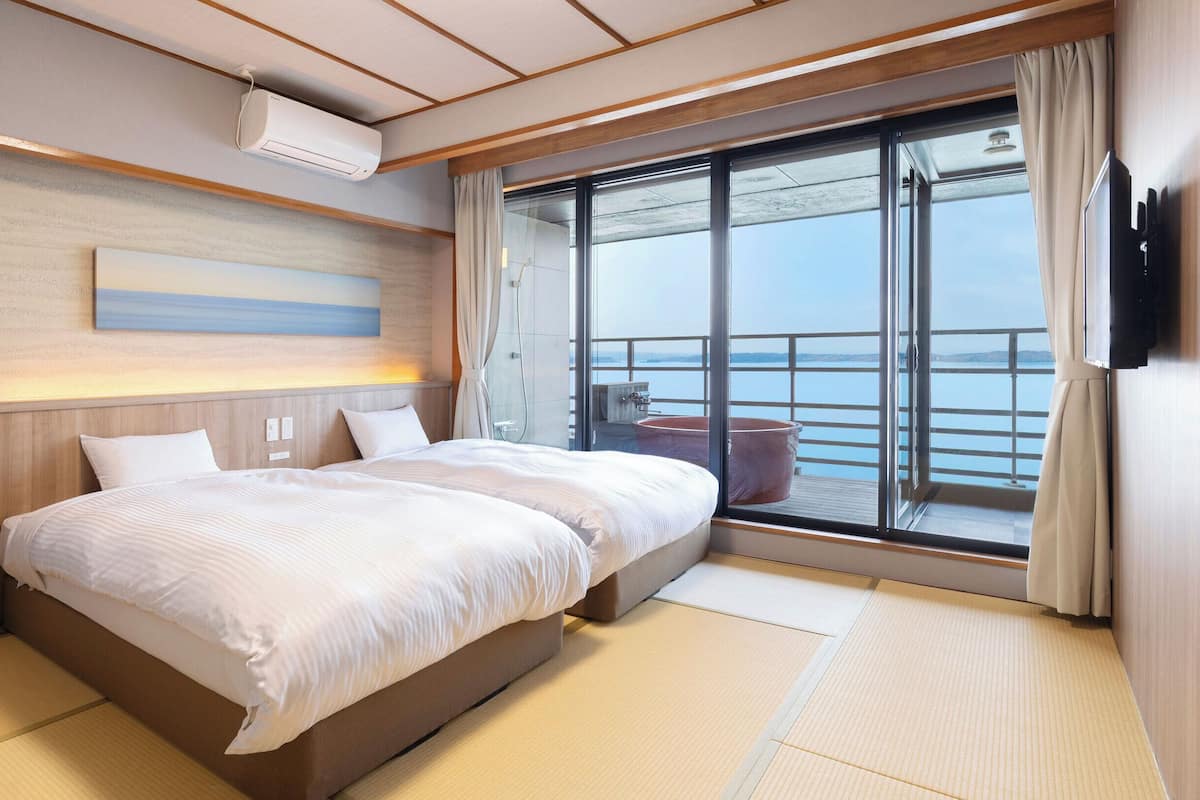 Une chambre d’hôtel moderne dotée d’un grand lit, offrant une vue sur la mer et donnant sur un espace extérieur grâce à une porte-fenêtre coulissante.