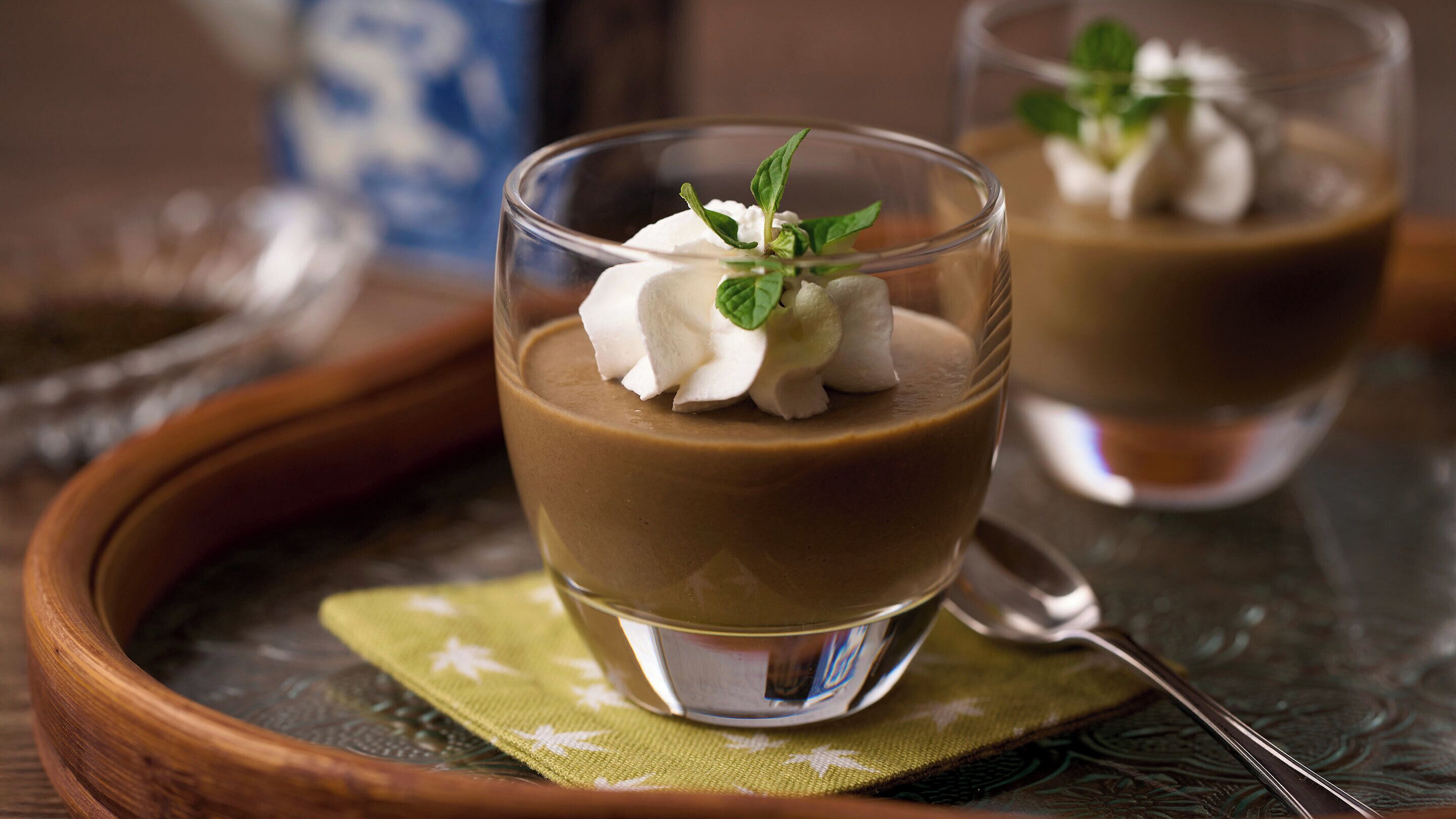 Zwei Dessertgläser mit Schlagsahne und Minzblättern auf einem Holztisch.