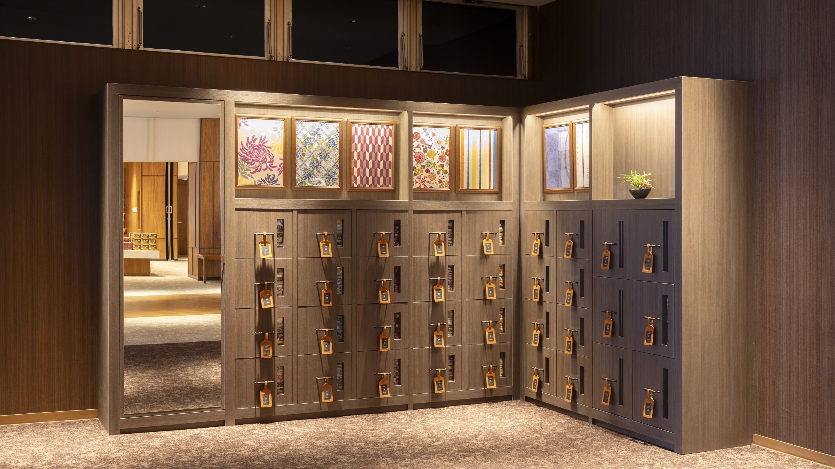 A hotel room with a large wooden wardrobe, multiple lockers, and a view of the hallway.