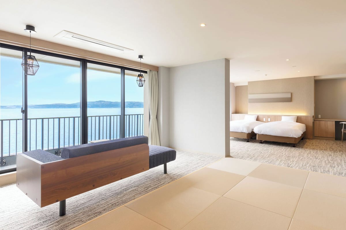 Une chambre d’hôtel moderne dotée d’un grand balcon, d’un canapé, d’un lit avec deux oreillers et d’un bureau.