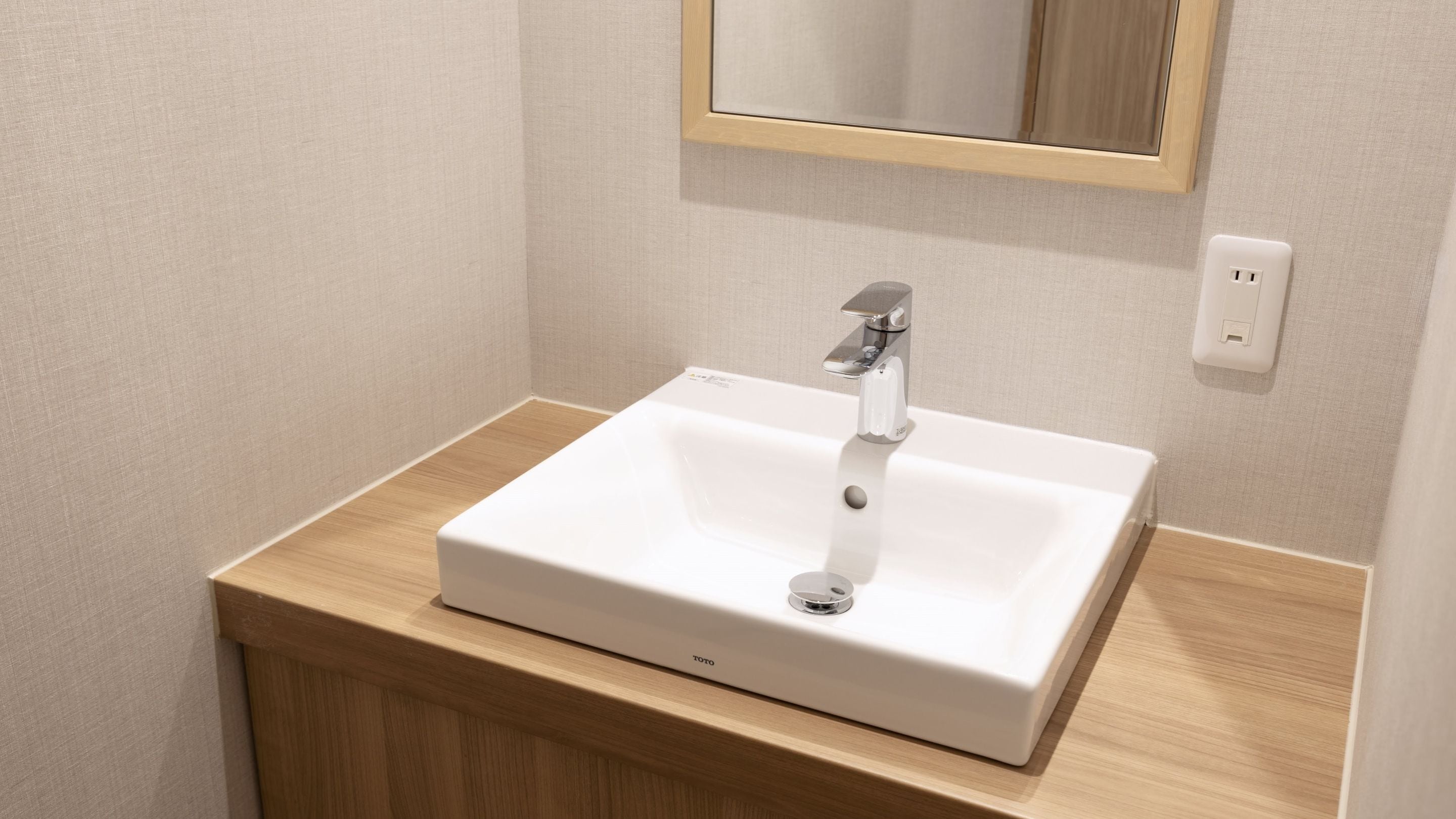 A bathroom with a white sink, wooden vanity, and a mirror above the sink.