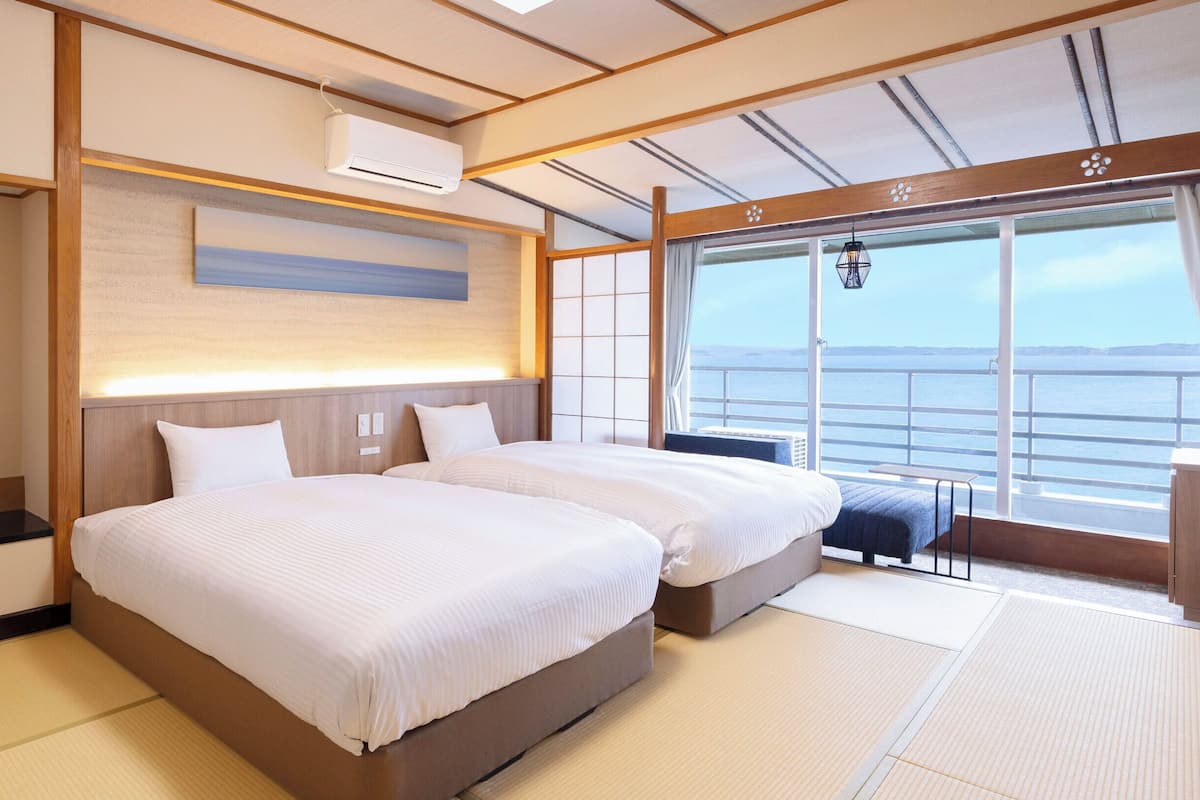 Une chambre d’hôtel avec deux lits, une grande fenêtre donnant sur la mer et un ventilateur de plafond.