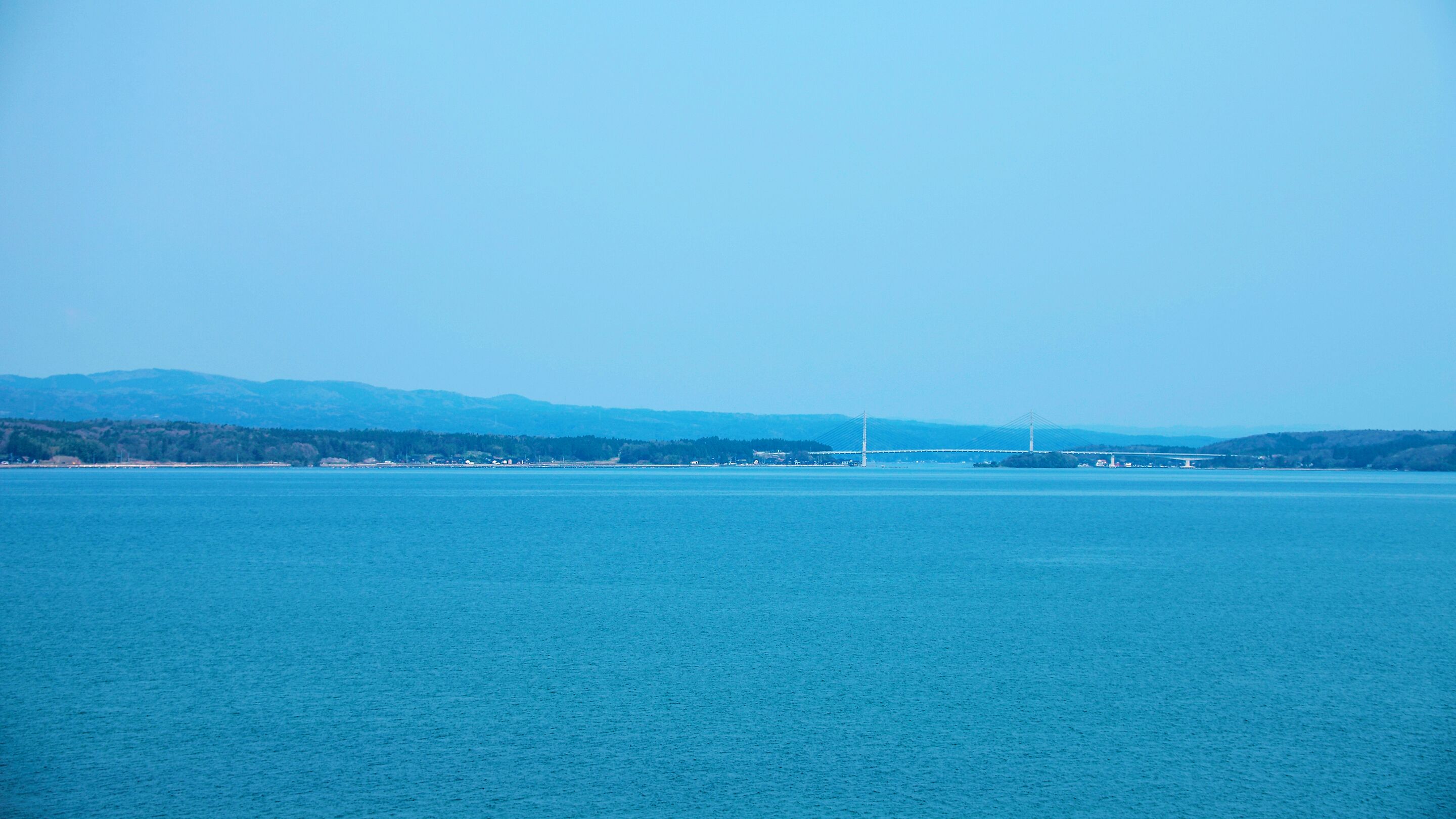A large body of water with a bridge in the distance and a hilly landscape in the background.
