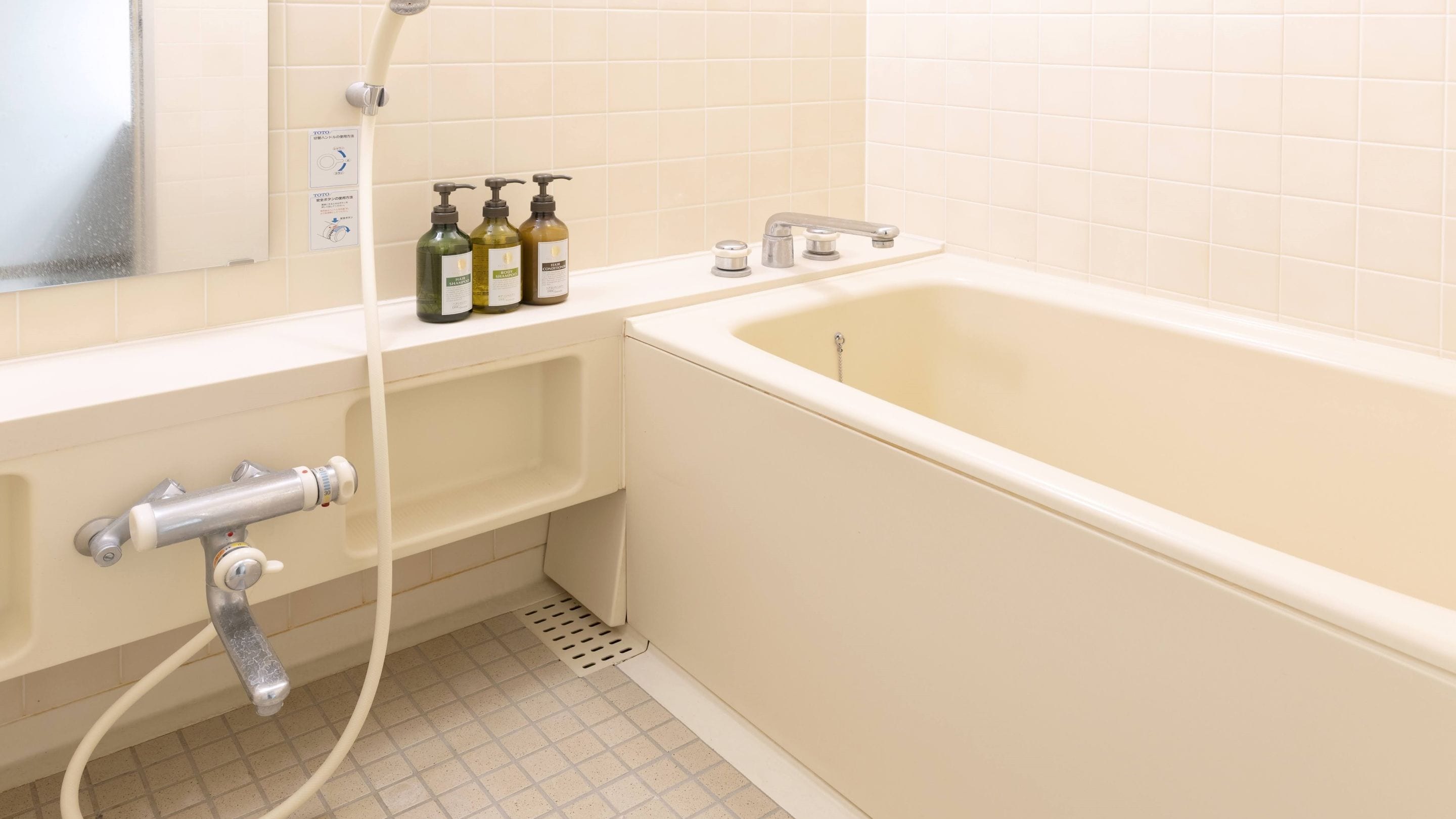 A bathroom with a bathtub, a shower, and a sink. There are three bottles on the edge of the bathtub.