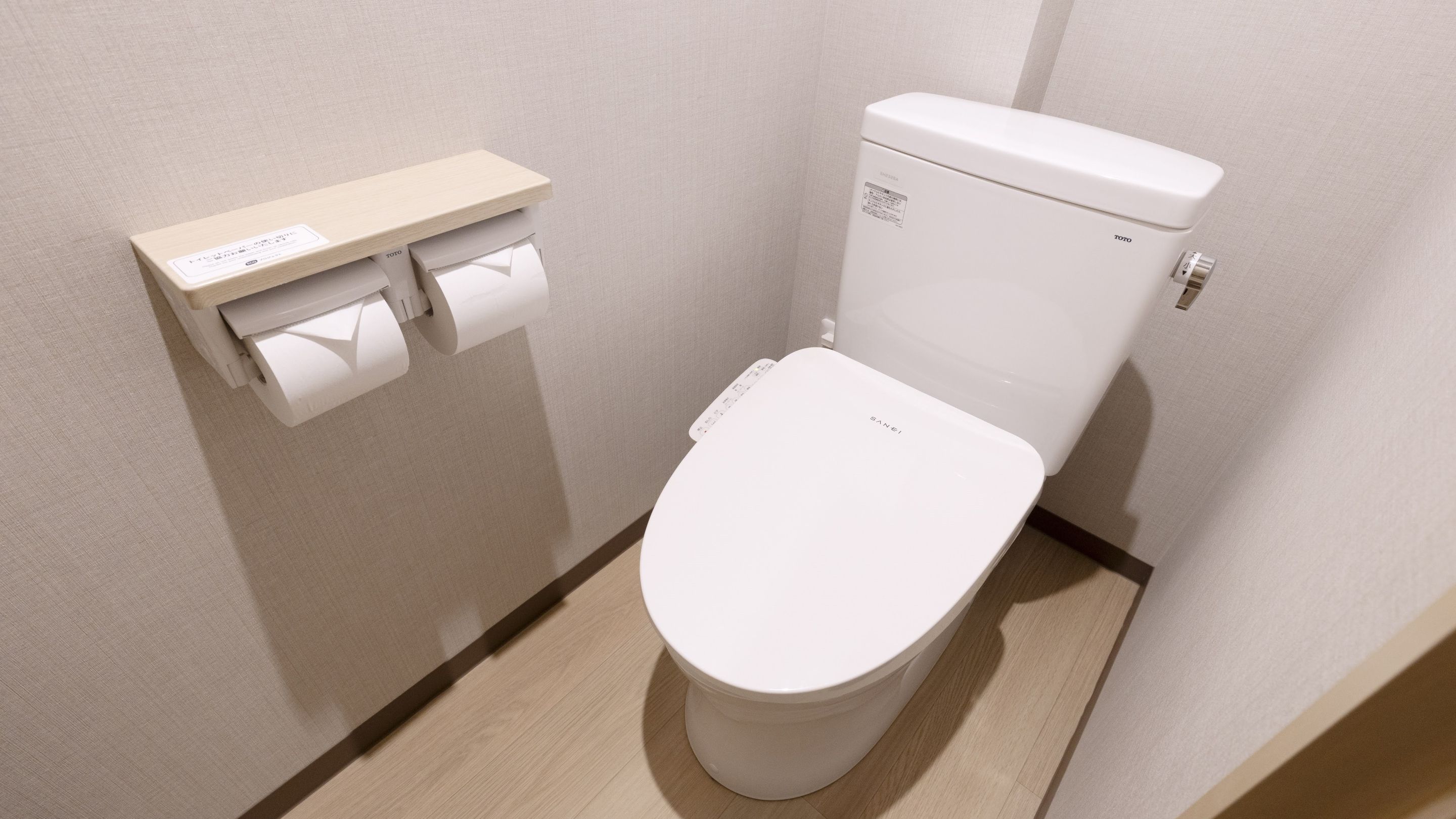 A modern toilet with a TOTO brand, a toilet paper holder, and a wall-mounted flush handle.