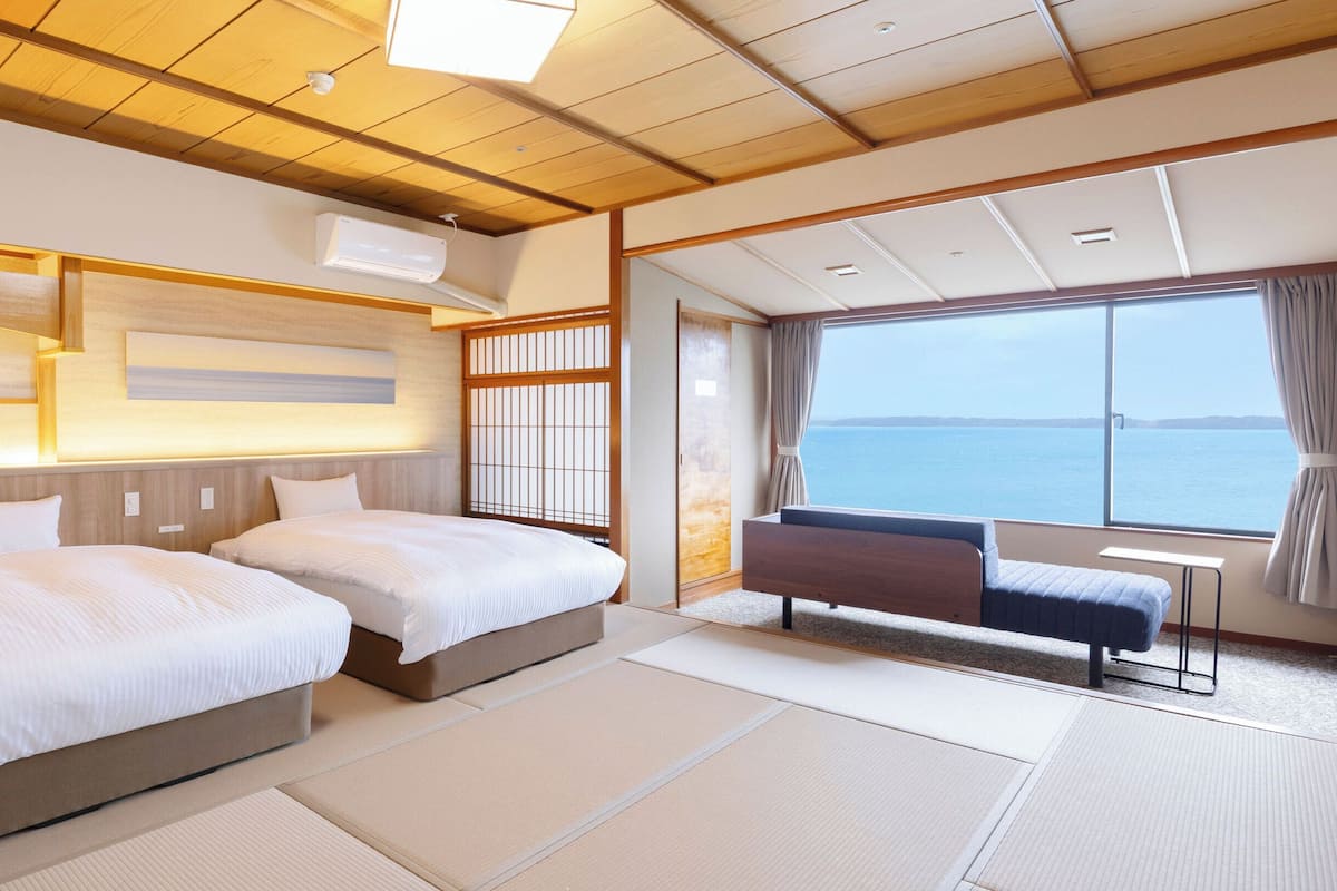 Une chambre d’hôtel avec deux lits, une vue sur la mer et une porte coulissante de style japonais traditionnel.