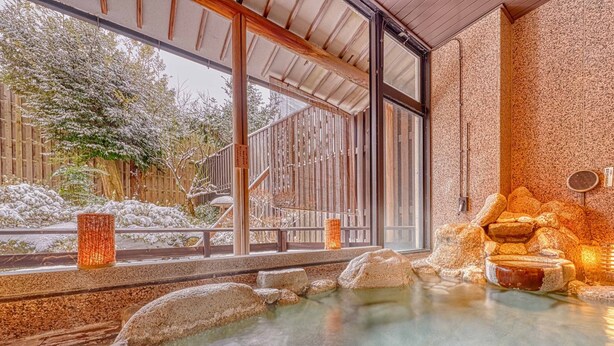 A traditional Japanese onsen with a stone bath, wooden railings, and a view of a snowy garden through large windows. - Ooedo Onsen Monogatari Wanwan Resort Awazu (Komatsu)