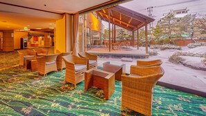 A hotel lobby with wicker furniture, a patterned carpet, and a view of a snowy outdoor area. - Ooedo Onsen Monogatari Wanwan Resort Awazu (Komatsu)
