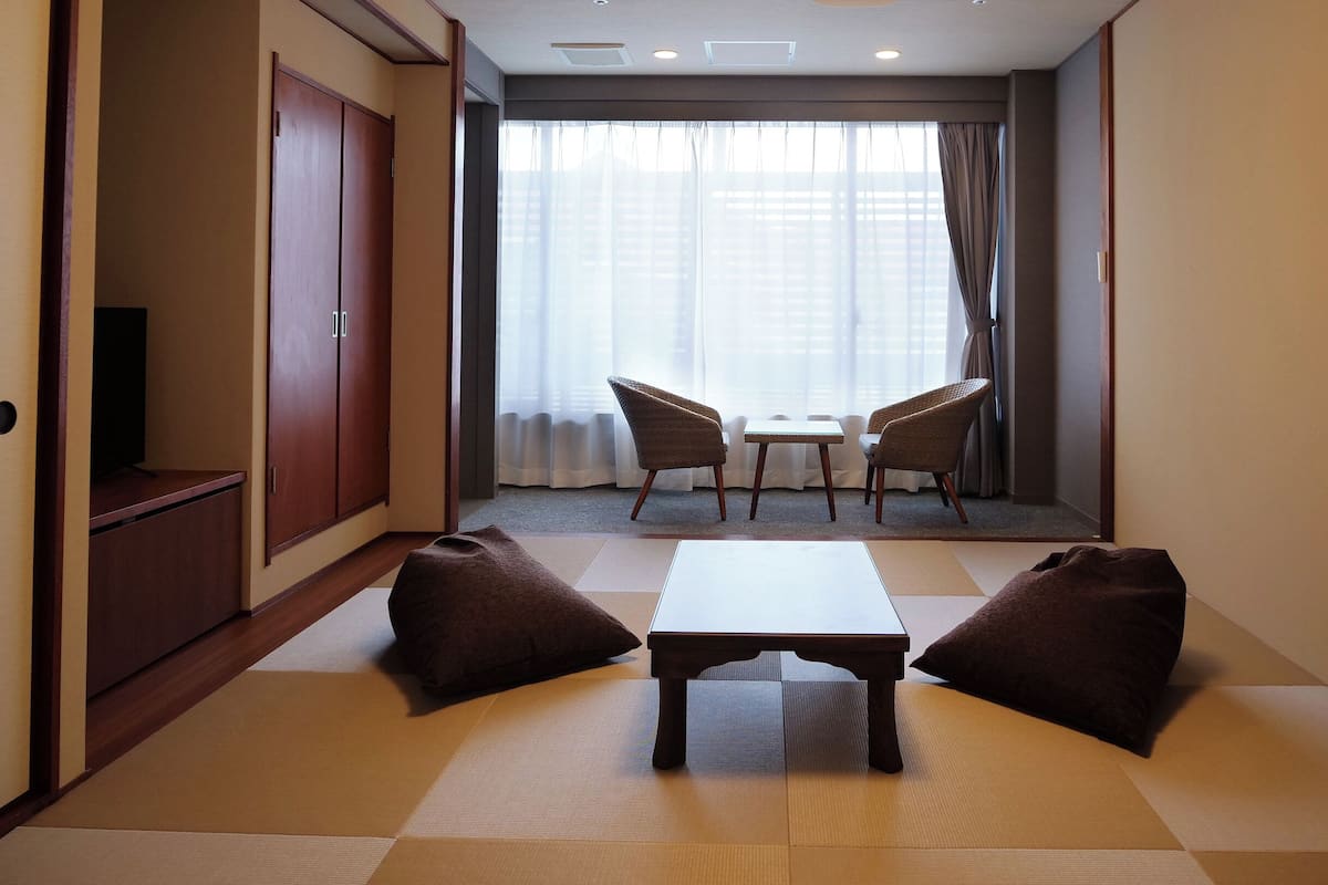 Una habitación con suelo de tatami, una mesa baja, dos sillas y un armario.