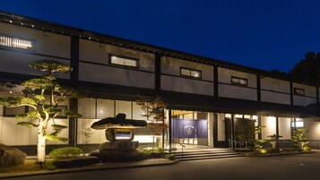 Un edificio tradicional japonés con un farol de piedra, un jardín bien cuidado y un letrero que indica que es un hotel.