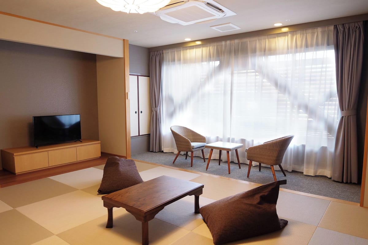 Habitación de hotel con televisor de pantalla plana, sofá, una mesita y una ventana con cortinas.