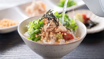 Un tazón de arroz con diferentes ingredientes, entre ellos cebolletas, algas marinas y una verdura roja.