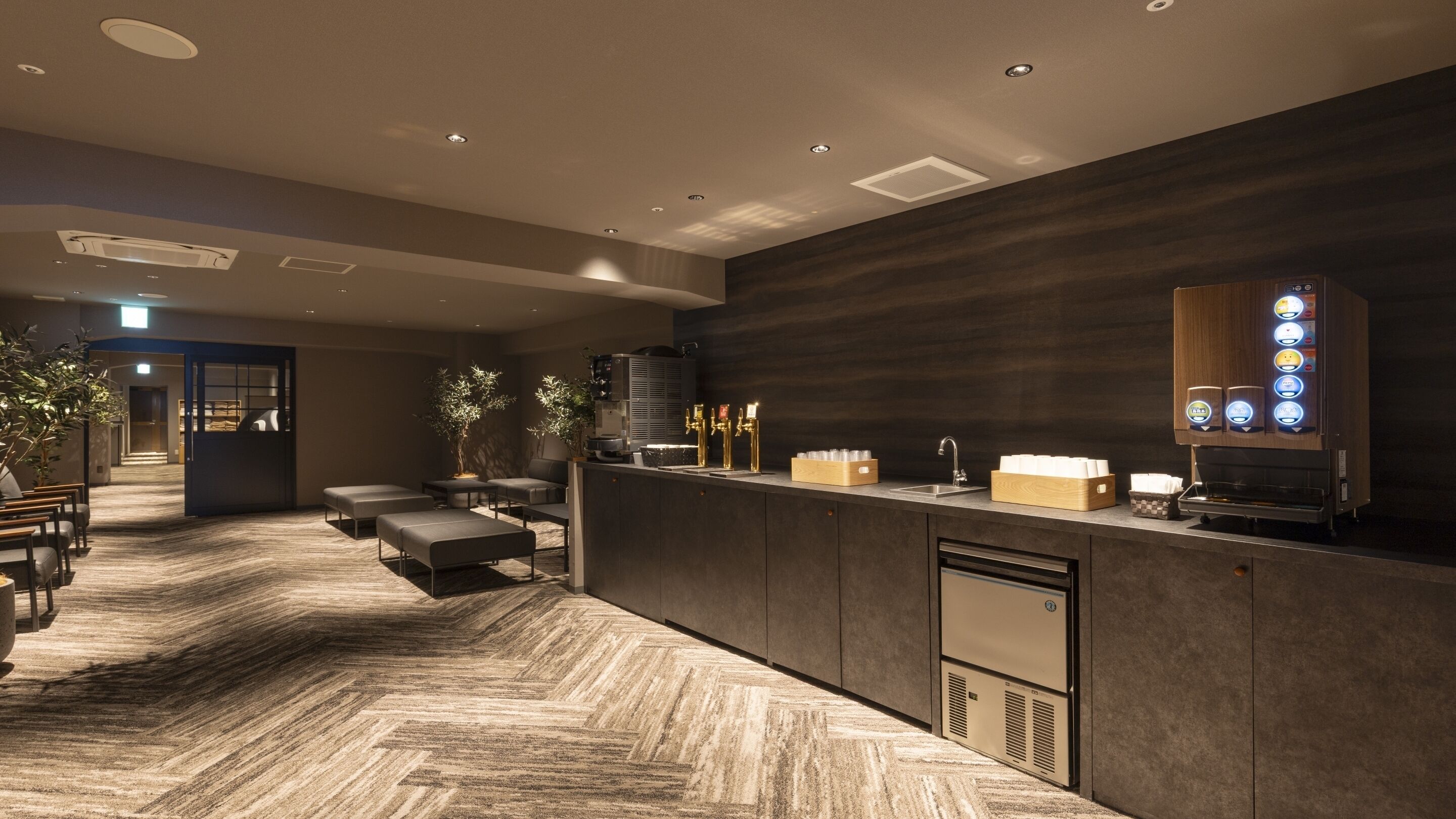A modern hotel lobby with a reception desk, seating area, and a coffee machine.