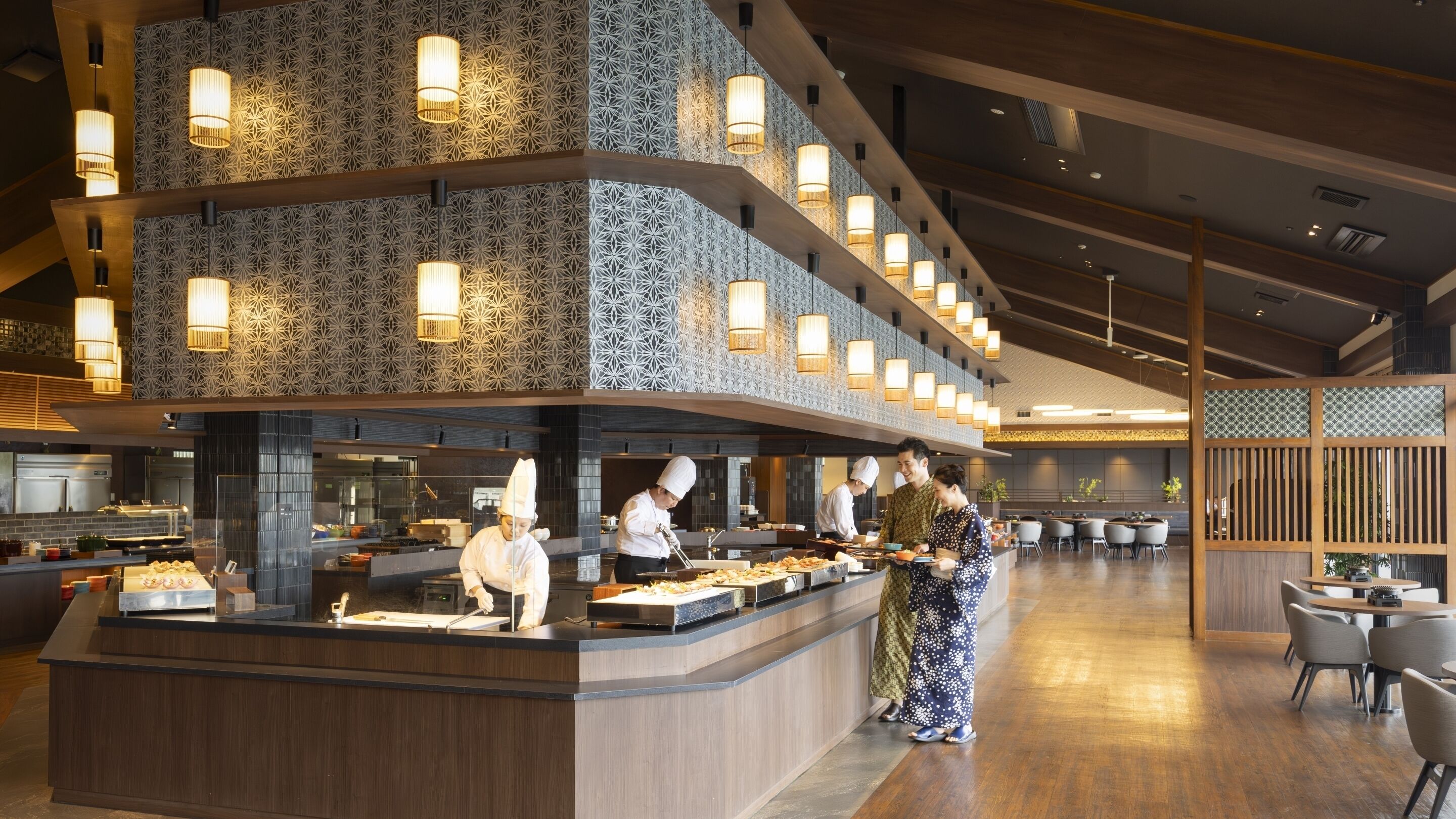 Un restaurante moderno con una barra central, cocineros preparando comida y una zona de estar con mesas y sillas.