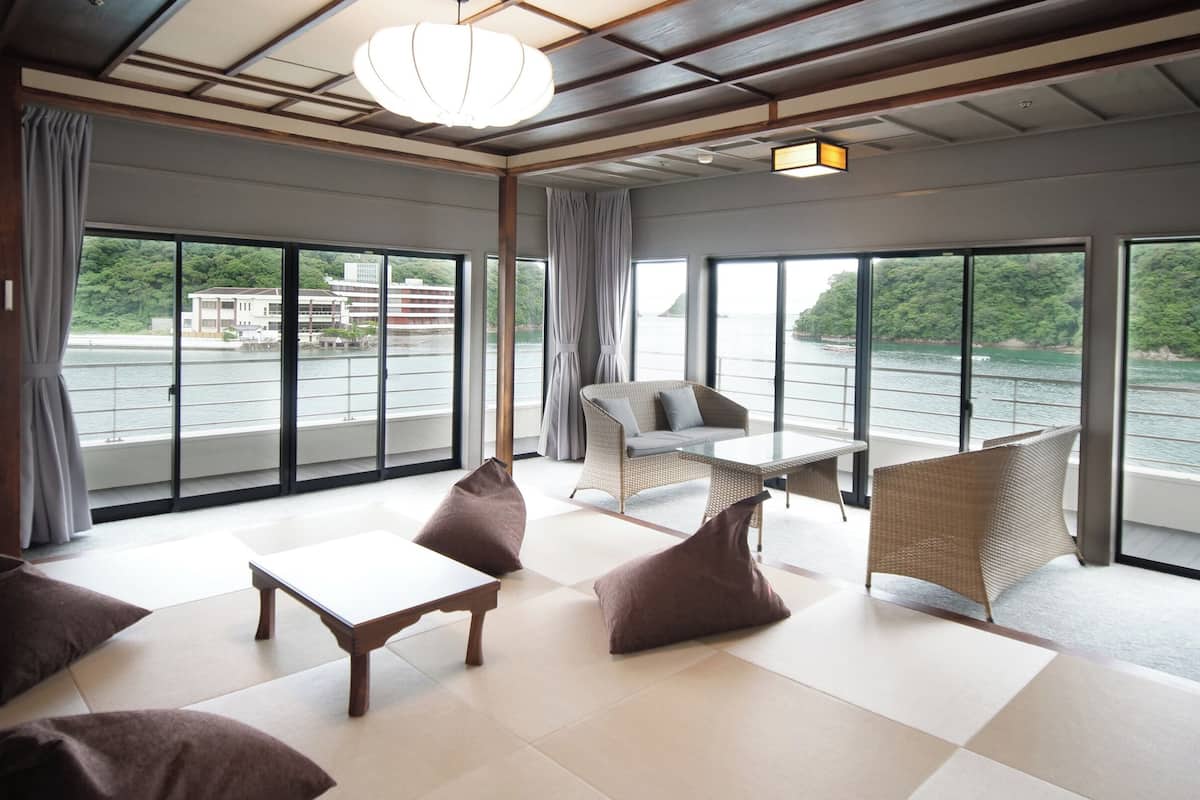 Amplia habitación con vista a un cuerpo de agua, que incluye un sofá, una mesa y una silla de mimbre.