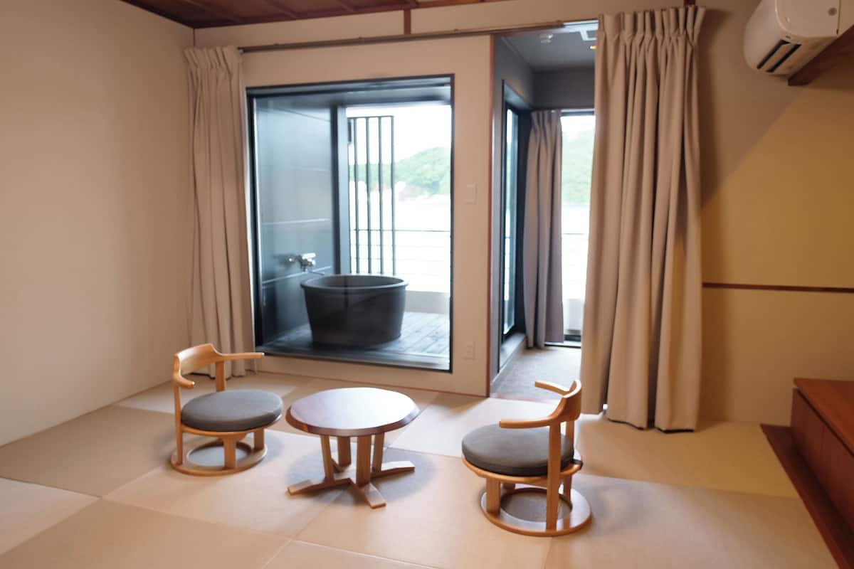 Una habitación con dos sillas de madera, una mesa redonda pequeña, un ventanal con vistas a un jacuzzi y una puerta corredera de vidrio.