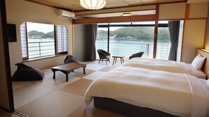 Habitación de hotel con una cama grande, una mesita, dos sillas y vistas a un cuerpo de agua y colinas.