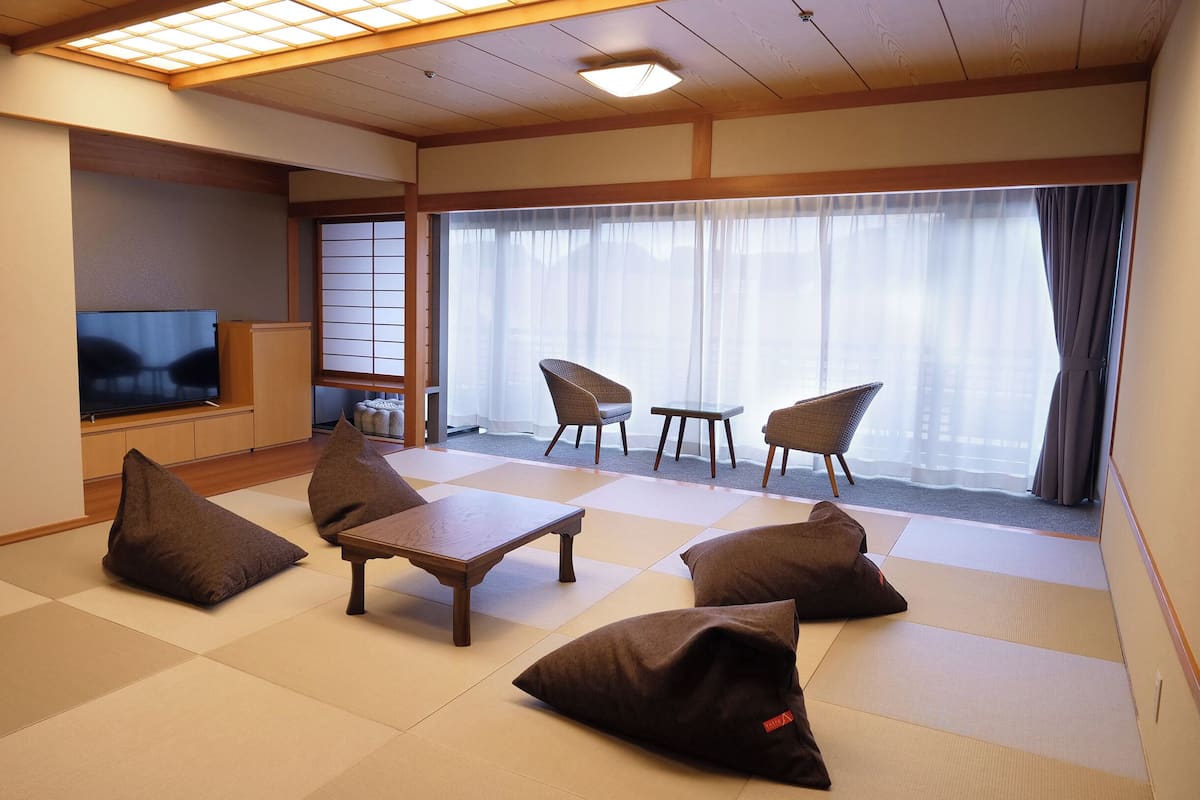 Una sala de estar tradicional japonesa con suelo de tatami, un televisor y dos sillones.