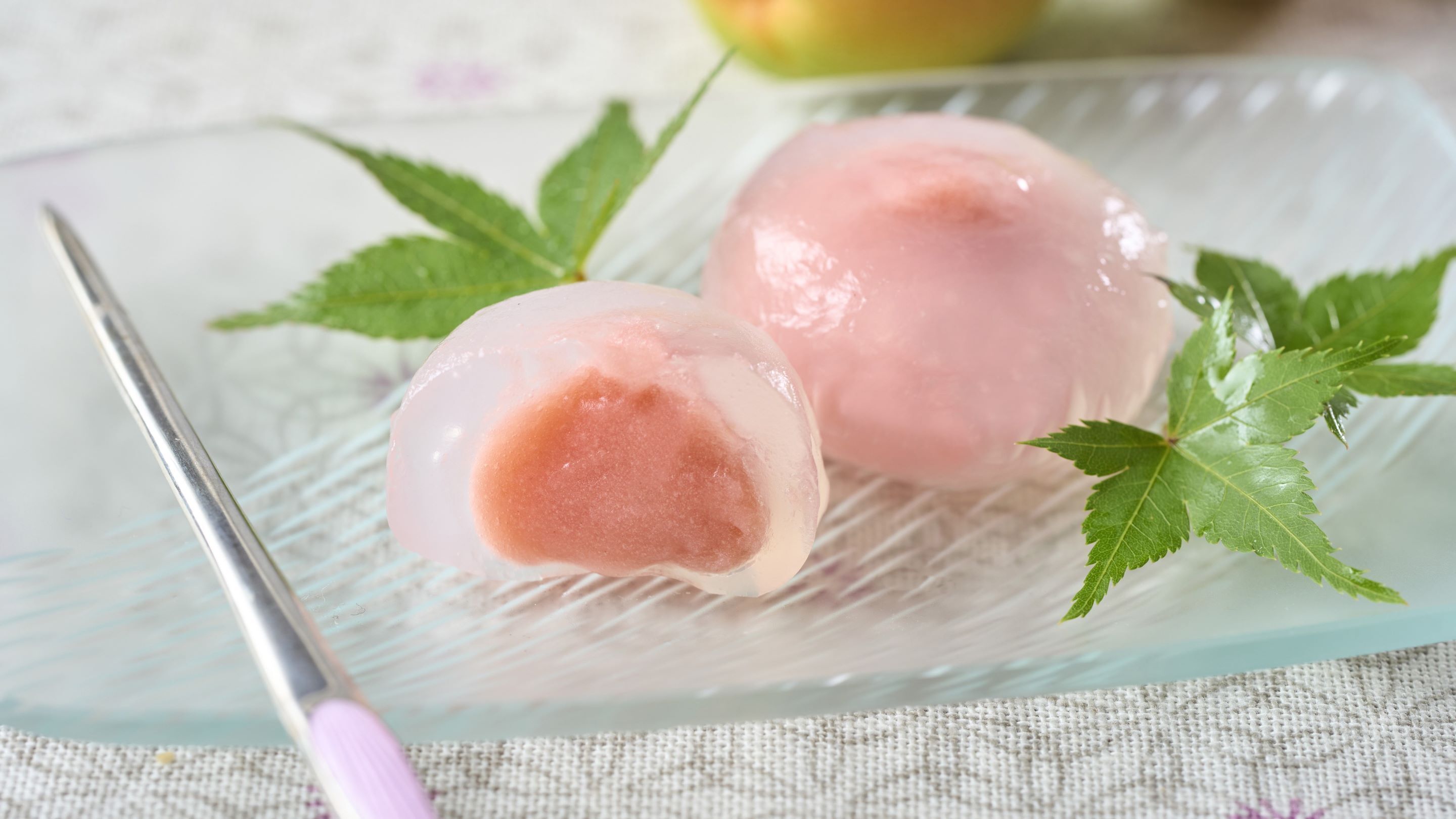 Dos bolas de helado rosa sobre un plato de vidrio, con un tenedor y hojas verdes.