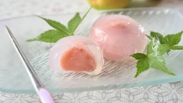Two pink ice cream balls on a glass plate with a fork and green leaves.