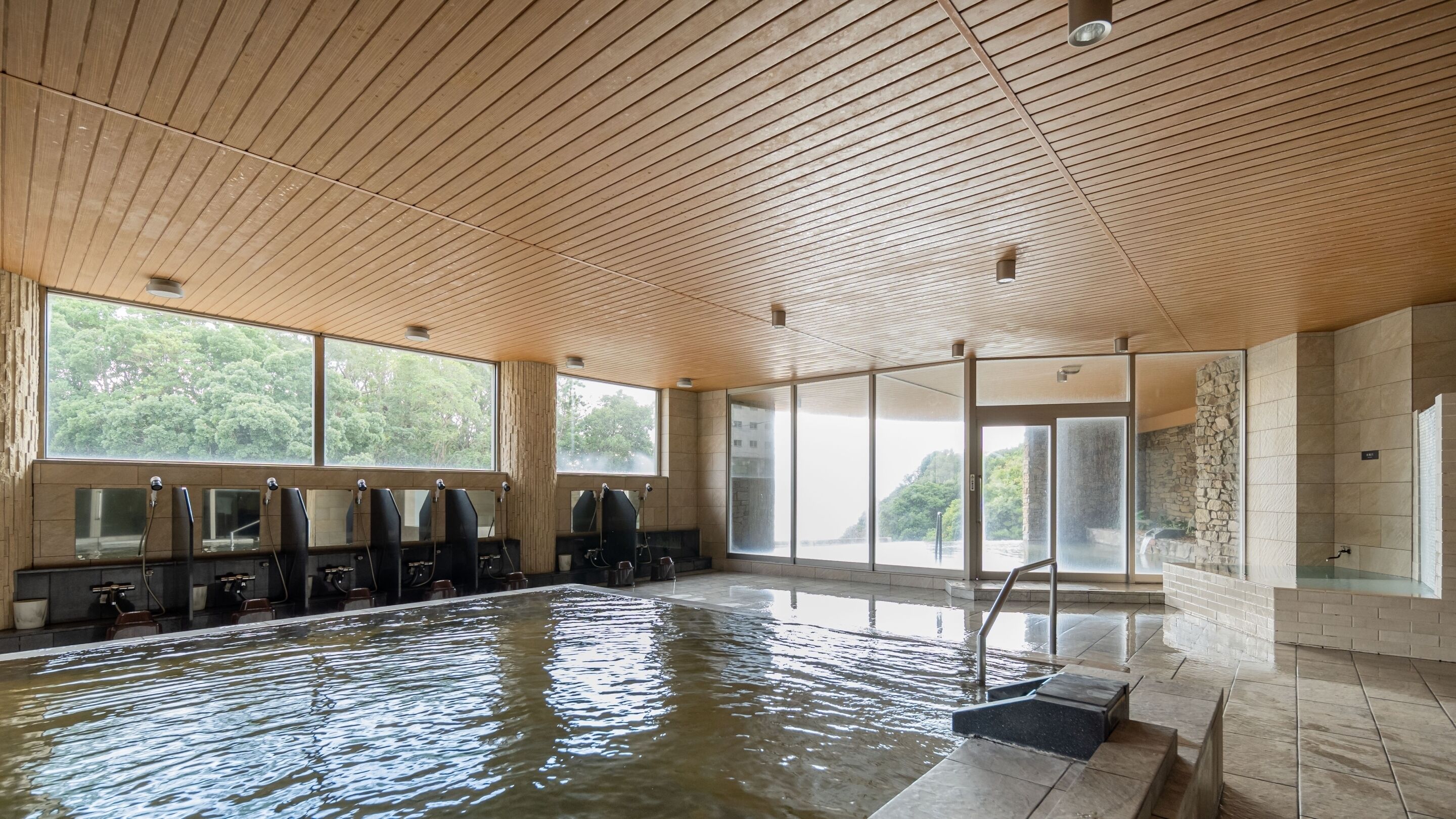 Une piscine intérieure avec un plafond en bois, de grandes fenêtres et des murs en pierre.