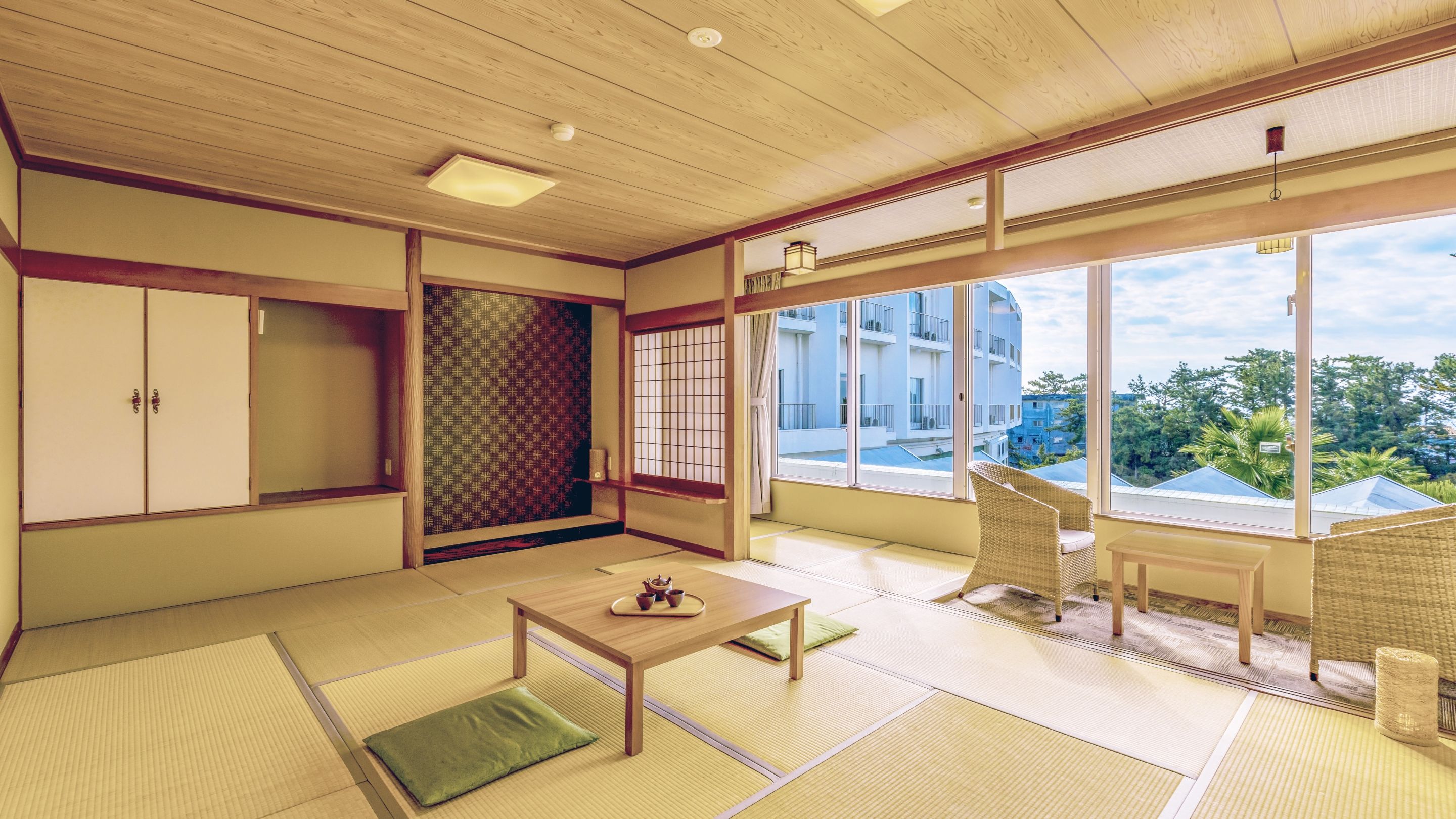A traditional Japanese room with tatami flooring, a sliding shoji screen, a wooden table with a tray, and a view of a residential building.