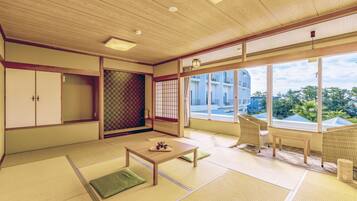 A traditional Japanese room with tatami flooring, a sliding shoji screen, a wooden table with a tray, and a view of a residential building.