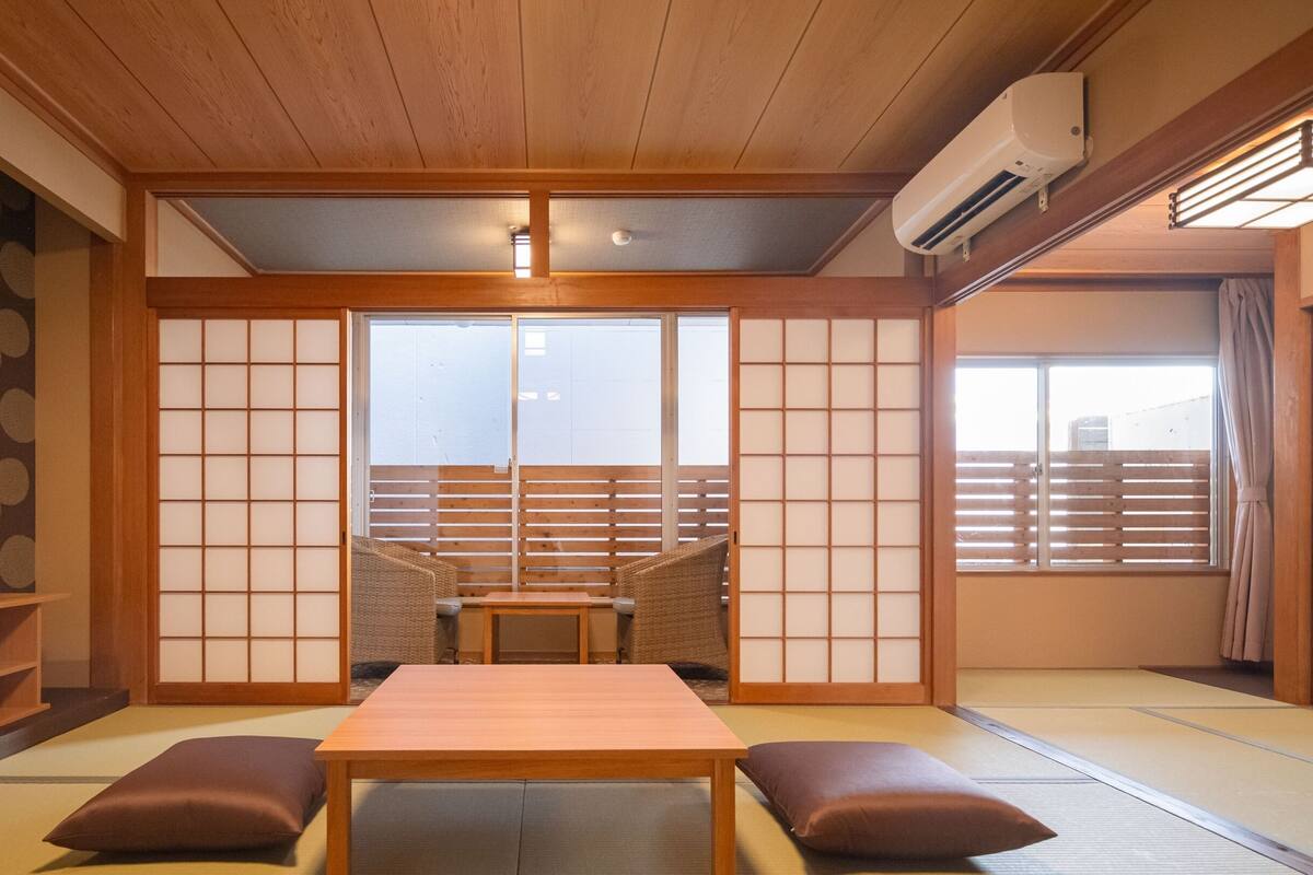 A traditional Japanese room with tatami flooring, a low table with cushions, a television, and sliding doors.