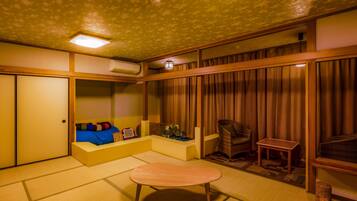 A traditional Japanese room with tatami flooring, a low table, a sofa with cushions, a chair, and a sliding door.
