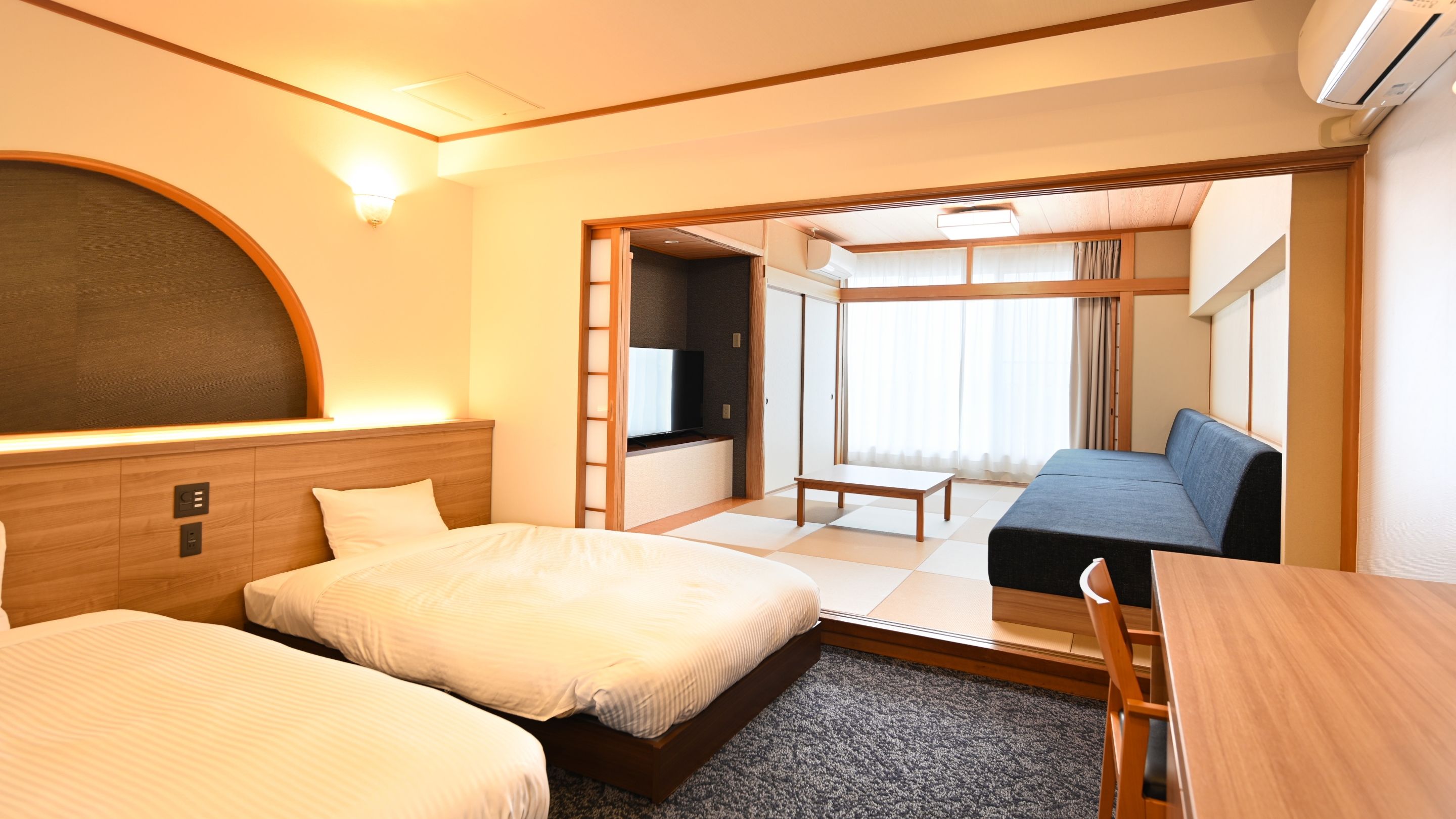 A hotel room with two beds, a sofa, a small table, and a TV.