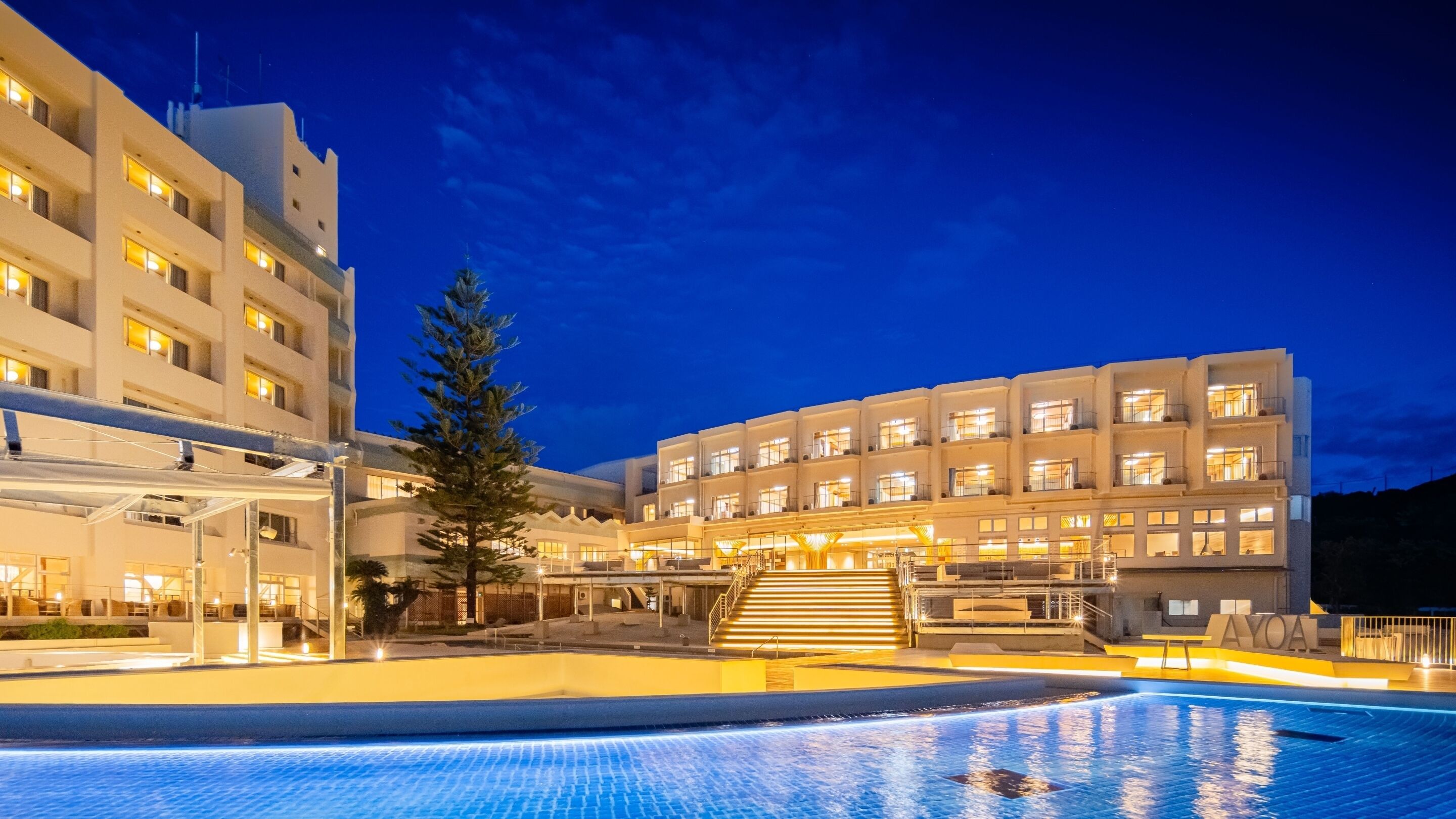 Un hotel con piscina, varios pisos y una fachada bien iluminada.