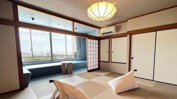 Una habitación con suelo de tatami, una puerta corredera, vistas a través de un ventanal grande y una lámpara en el techo.