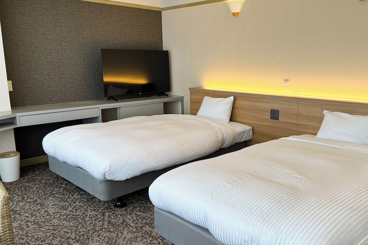 Une chambre d’hôtel avec deux lits, une télévision et un petit bureau.