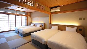Habitación de hotel con dos camas, esteras de tatami, un ventilador de techo y vistas al exterior.