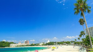 A beach with clear turquoise water, palm trees, and a hotel in the background.