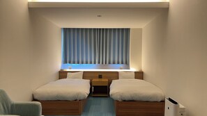 Quarto de hotel com duas camas, uma janela com cortinas, uma mesinha de cabeceira e um criado-mudo.