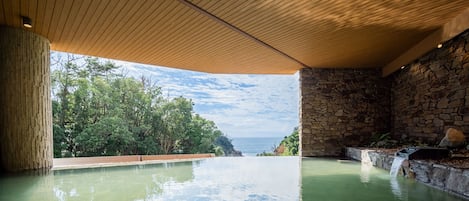Piscina infinita con vista al océano, rodeada de muros de piedra y techo de madera.