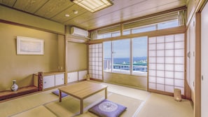 A traditional Japanese room with tatami flooring, a low wooden table, a cushioned bench, and a large shoji screen with a view of buildings and the sea. - TAOYA Shirahama Senjyo (Shirahama)