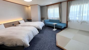 A hotel room with two beds, a sofa, a small table, and a window with curtains.