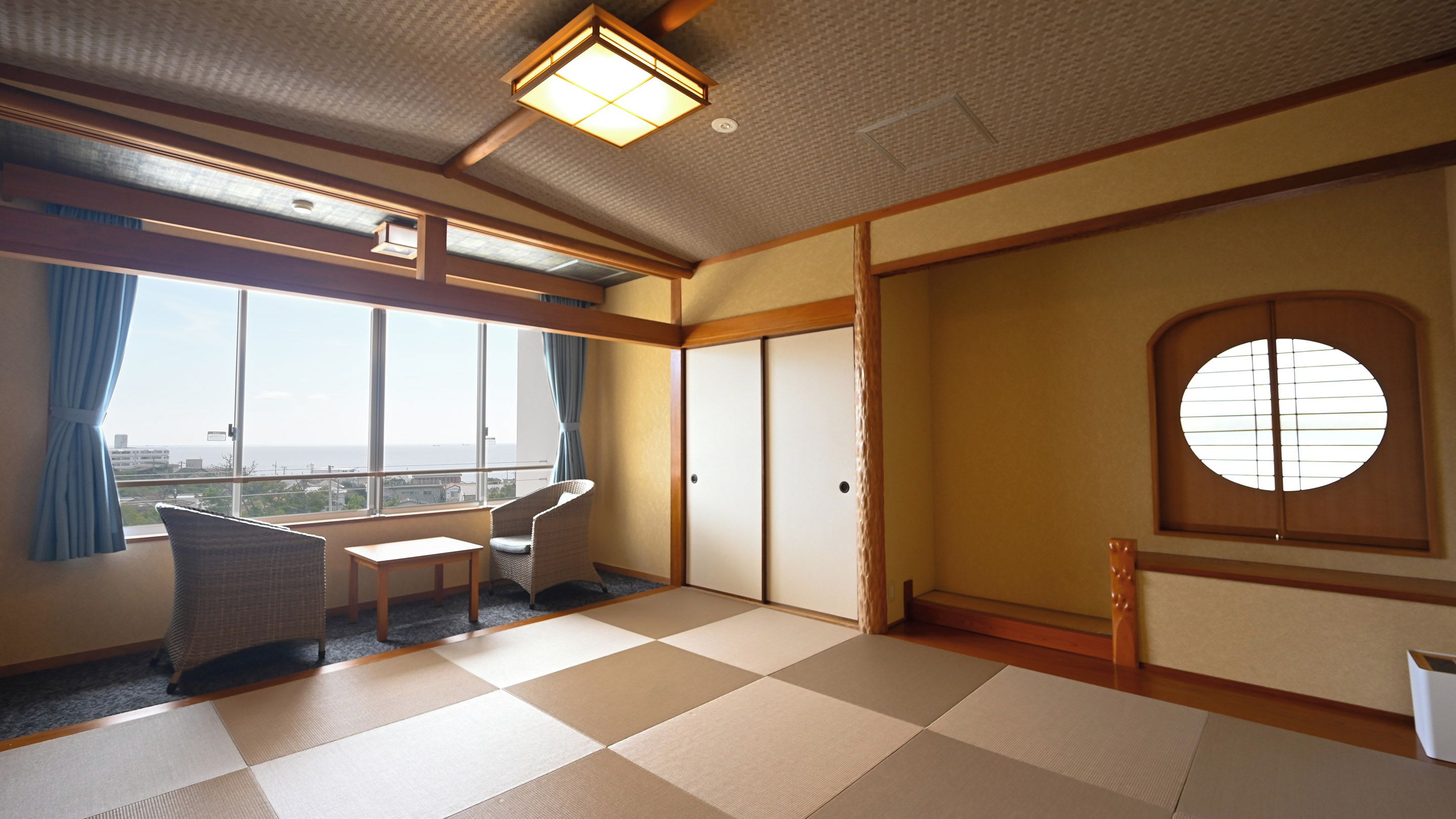 Una habitación con suelo de tatami, una puerta corredera japonesa tradicional, vista al mar y una pequeña mesa con sillas.