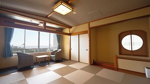 Een kamer met tatami vloer, een traditionele Japanse schuifdeur, uitzicht op zee en een kleine tafel met stoelen.