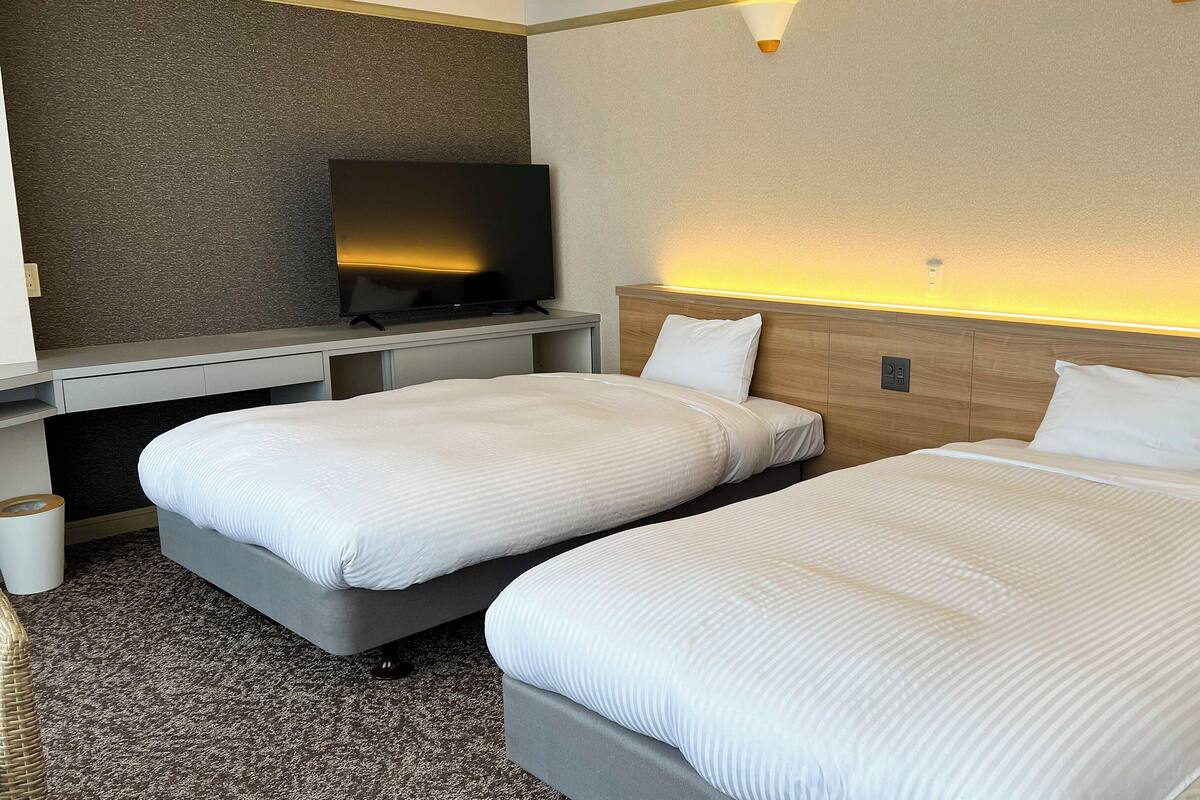 A hotel room with two beds, a TV, and a small desk.