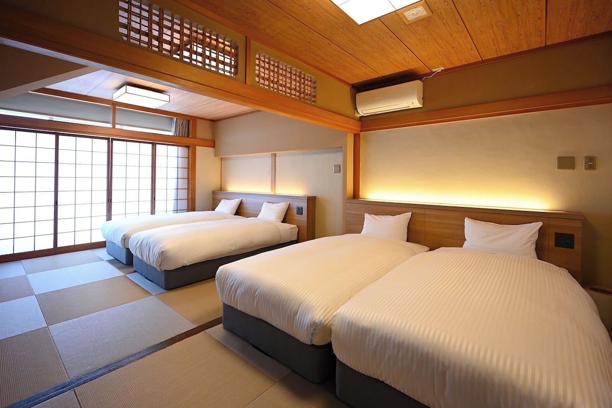 A hotel room with two beds, tatami mats, wooden beams, and a traditional Japanese-style ceiling.
