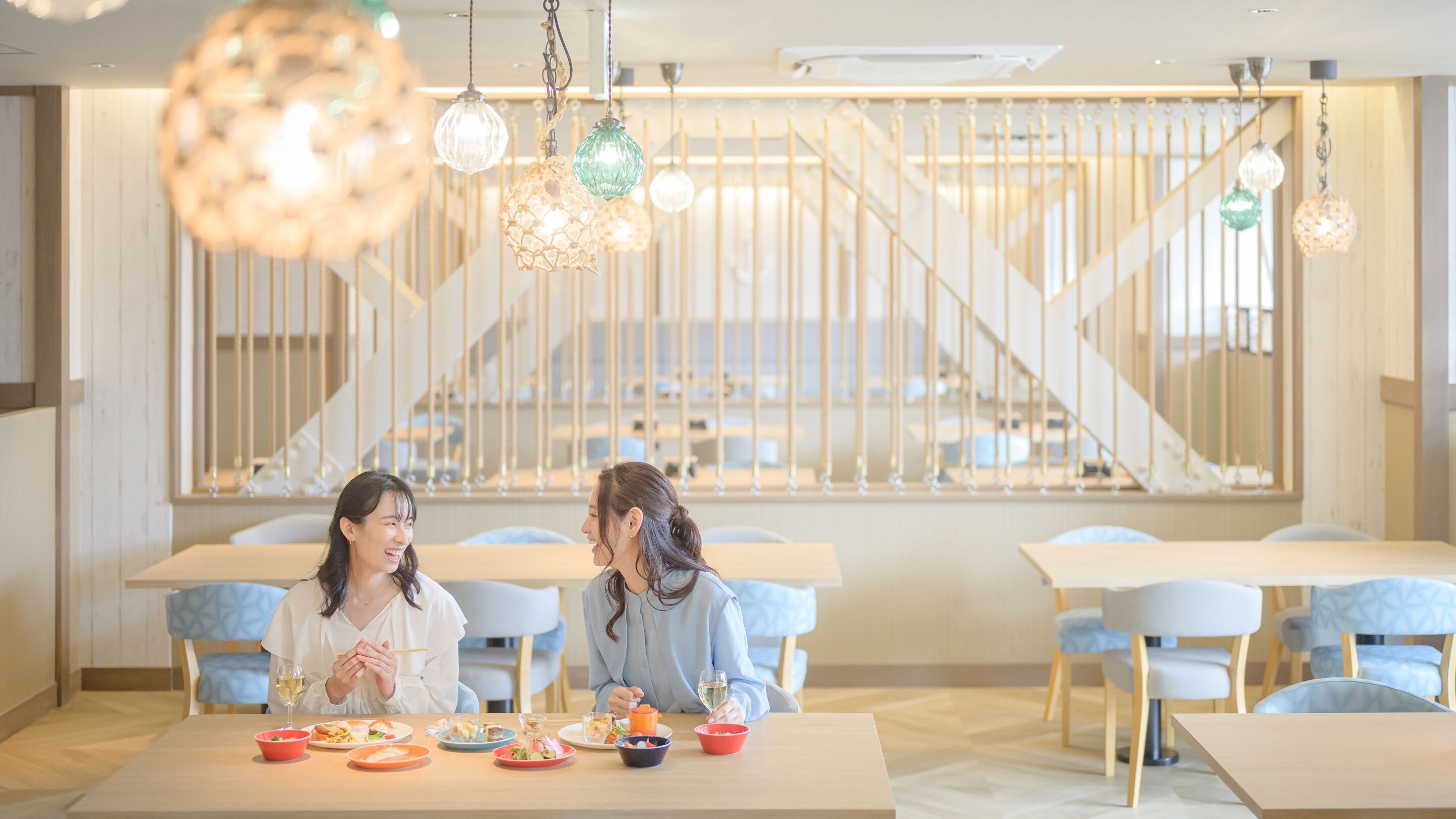 A dining area with tables and chairs, a staircase in the background, and hanging pendant lights.